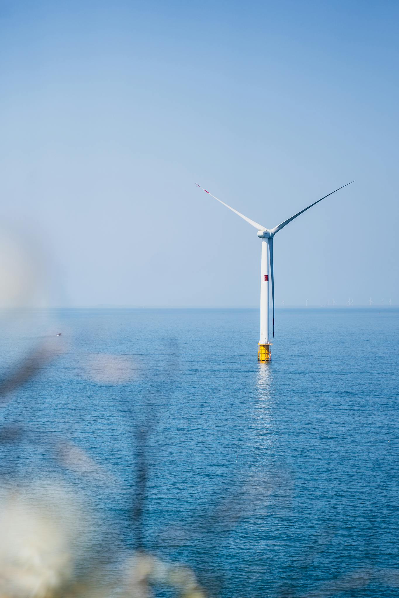 A single offshore wind turbine stands in peaceful ocean waters, captured on a clear day.