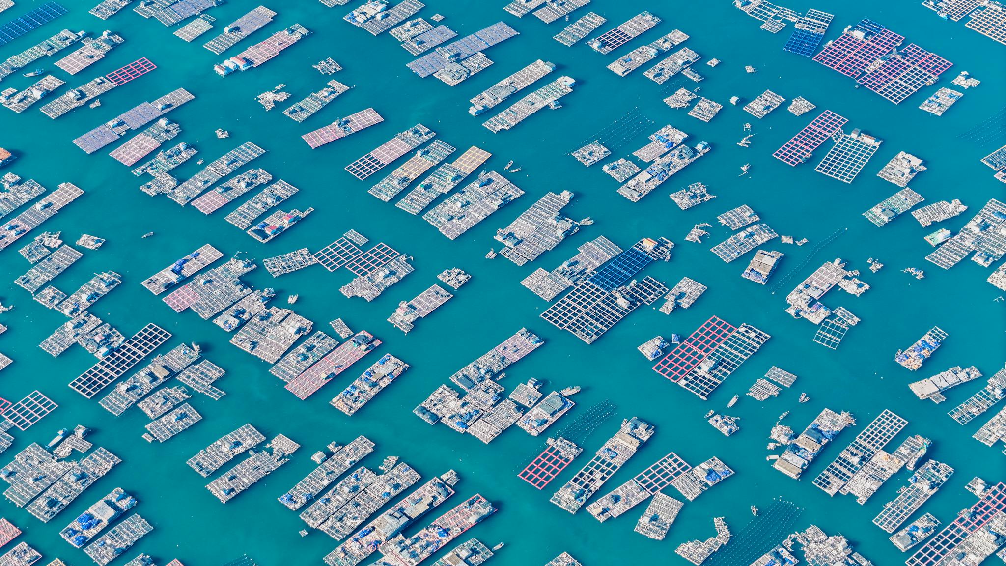 Aerial photo capturing extensive fish farms with grid-like structures in deep blue waters.
